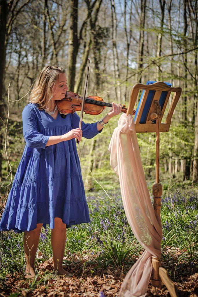 Jennifer playing violin in a bluebell wood