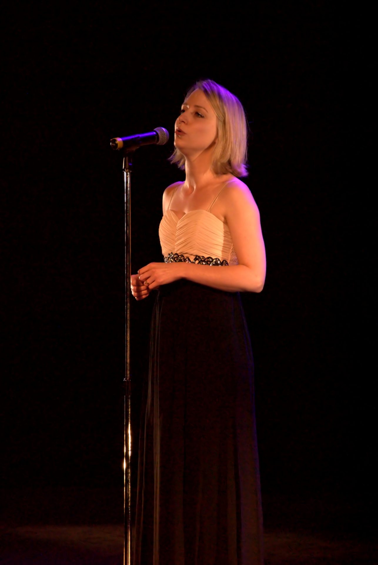 Jennifer Maslin singing into a microphone against a black backdrop