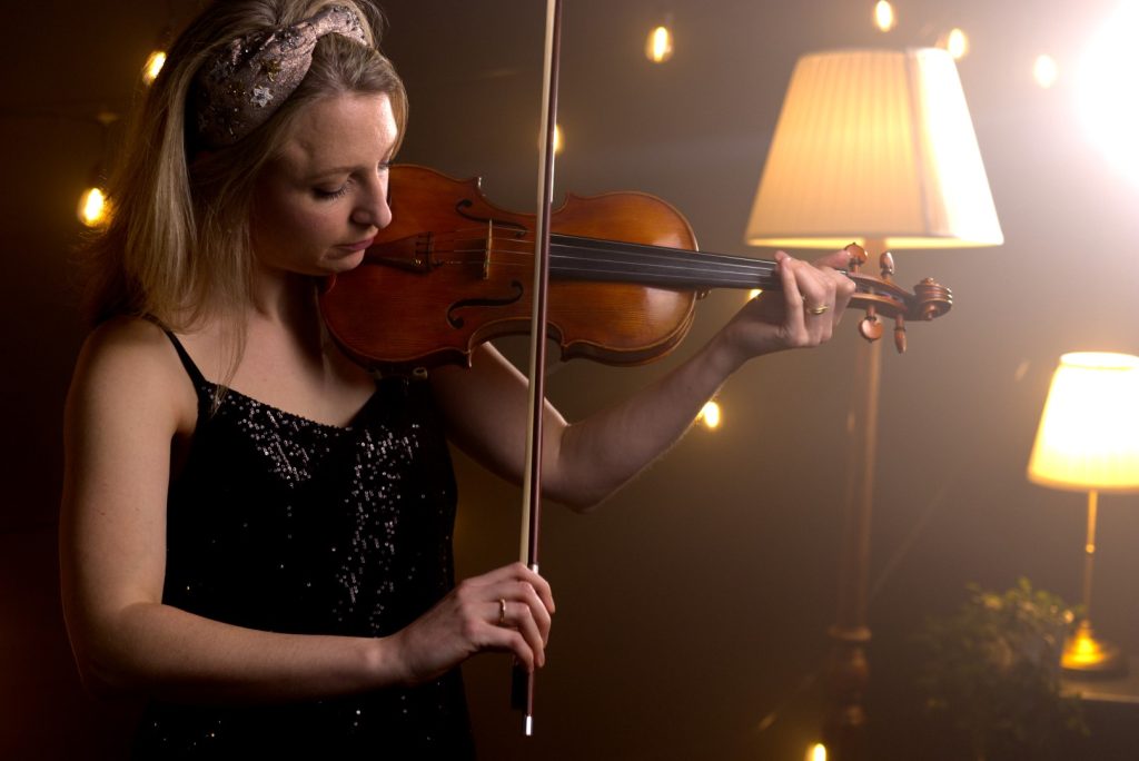 Jennifer Maslin playing violin with a standard lamp in the background